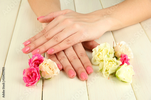 Woman hands with pink manicure and flowers, on wooden