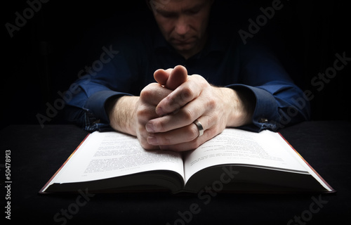 Man praying to God with his hands resting on a bible.