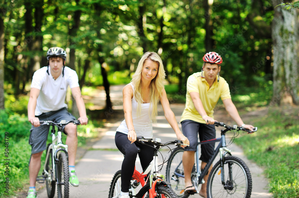 Portrait of attractive young woman on bicycle and two men in blu
