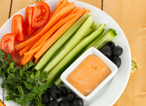 Assorted raw vegetables sticks in plate on wooden table close