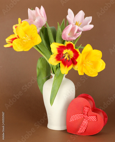 Beautiful tulips in bucket with gift on brown background