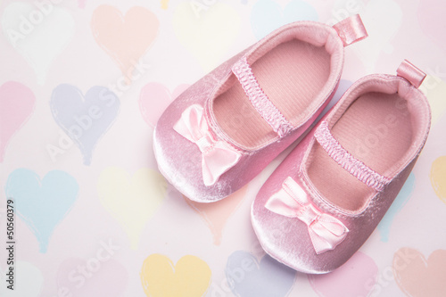 Baby pink booties on heart pattern background