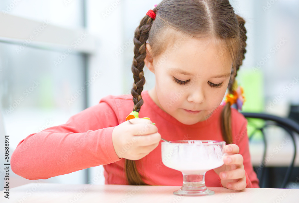 Fototapeta premium Little girl is eating ice-cream in parlor