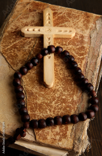 Bible, rosary and cross on wooden table close-up
