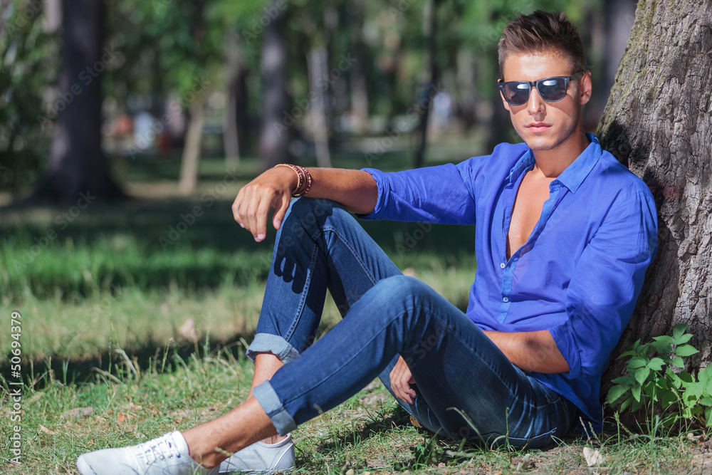 Fototapeta premium serious man sits on ground next to tree