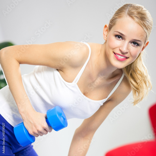 Young happy smiling woman with dumbbells, indoors