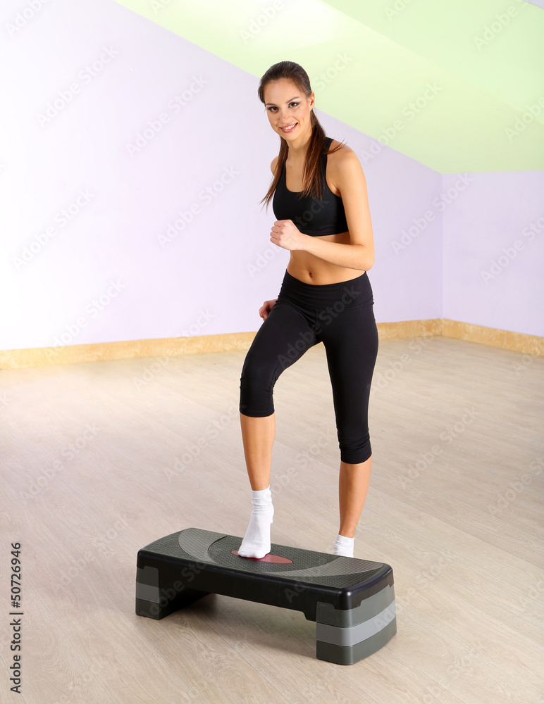 Young woman doing fitness exercises on stepper at gymnasium