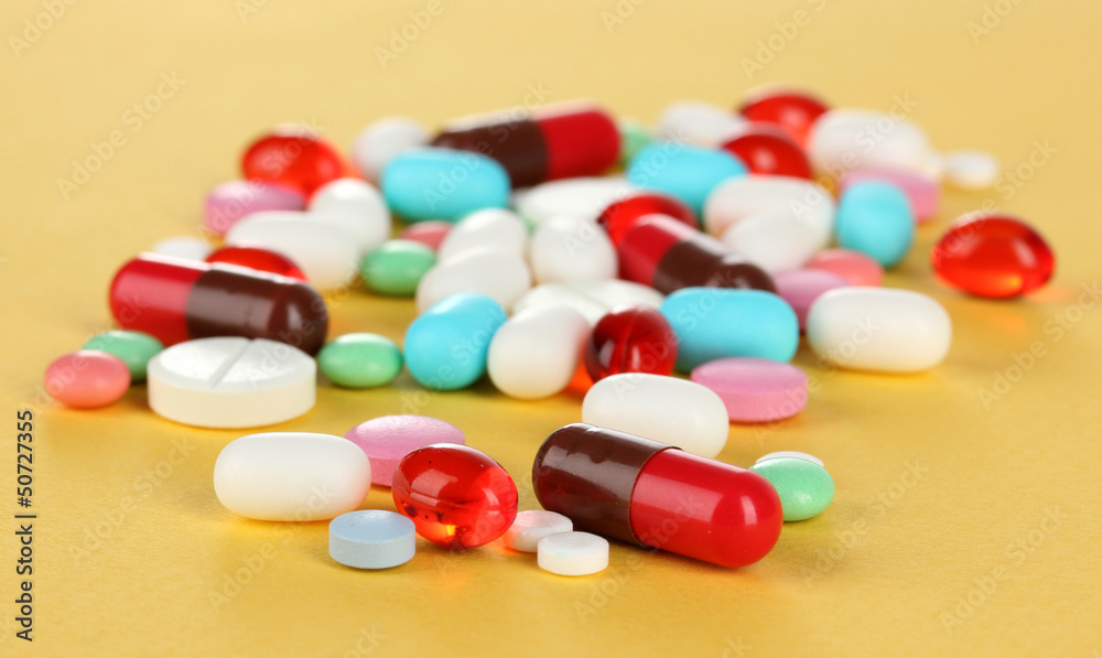 Assortment of pills, tablets and capsules on yellow background