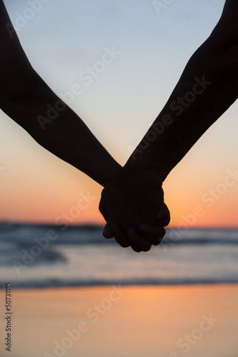 Young couple holding hands on the sea beach at sunset