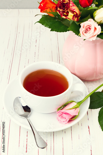 Cup of tea on wooden table with rose flowers
