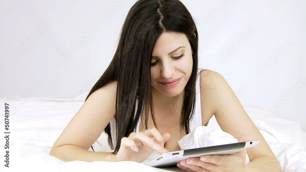 Happy woman writing email on tablet in bed Happy woman writing email on tablet in bed