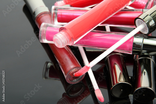 beautiful lip glosses with rose petals, on grey background