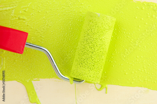 Paint roller brush with green paint, on wooden background