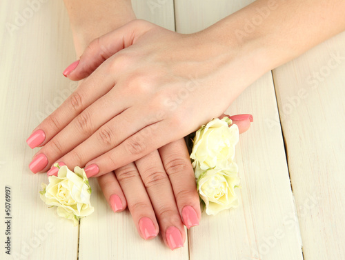 Woman hands with pink manicure and flowers, on wooden
