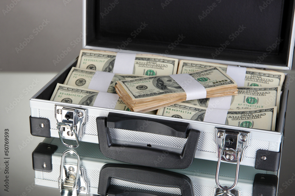 Suitcase with 100 dollar bills on grey background