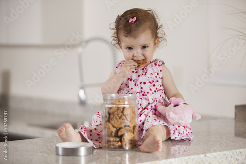 Foto Cute little girl eating cookies from a jar