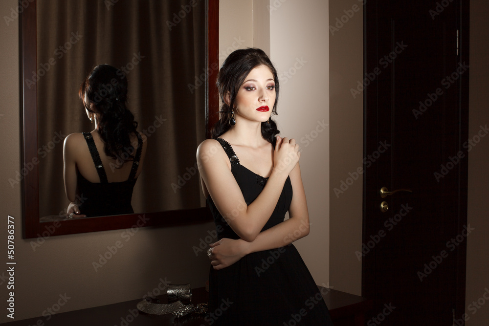 Attractive young woman in black dress standing in hotel room
