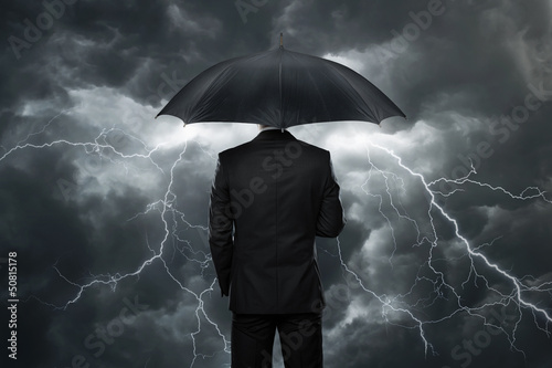 Businessman with umbrella standing in front of storm