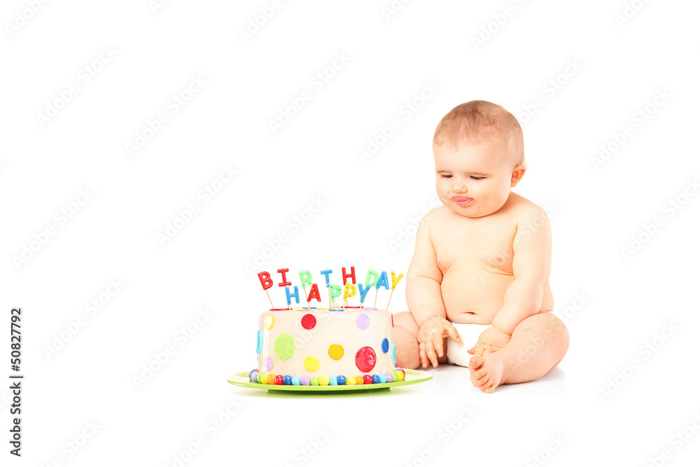 A 9 month old baby in diapers sitting next to a birthday cake A 9 month old baby in diapers sitting next to a birthday cake