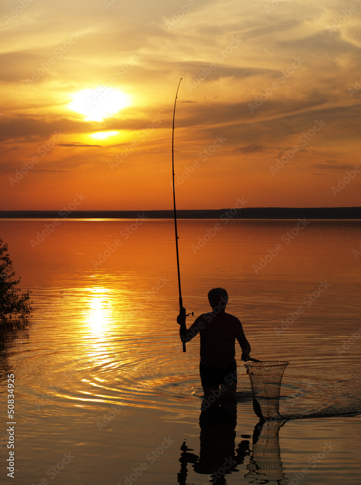 Fisherman catches fish by spinning on the lake at sunset