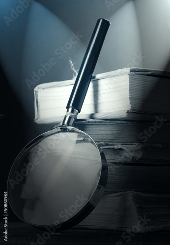 Magnifying glass over the stack of books in dark grey light