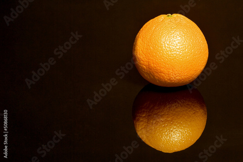 Eine Orange spiegelt sich auf schwarzer Flaeche photo