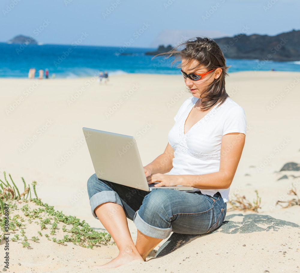Woman sitting on beach with laptop