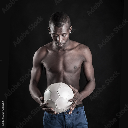 Young African man with a white soccer ball on black background. © pio3