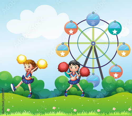 Two cheerers dancing in the hill with a ferris wheel at the back