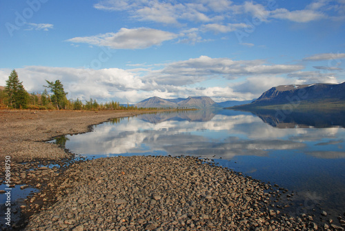 Lake Lama and reflected in the water clouds and mountains of the