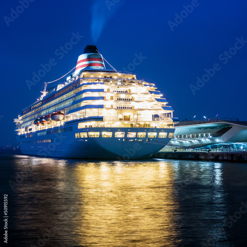 Fotografie Huge luxury cruise ship putting off from pier at night.
