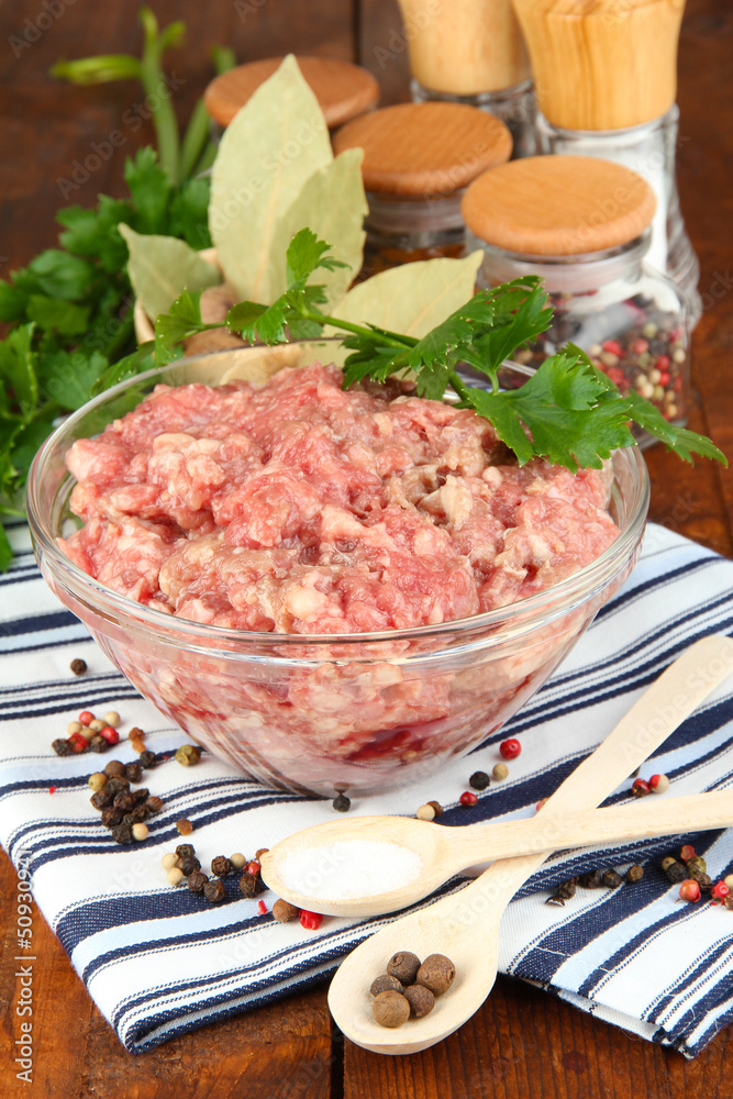 Bowl of raw ground meat with spices on wooden table