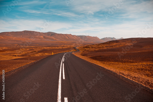 Highway through dry gravel lava field landscape under a blue sum