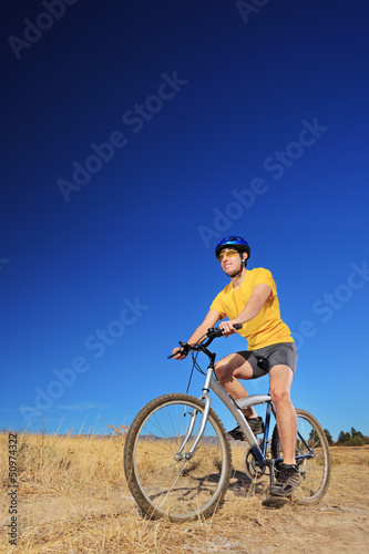 Fototapeta Naklejka Na Ścianę i Meble -  A young male with yellow shirt and helmet riding a mountain bike