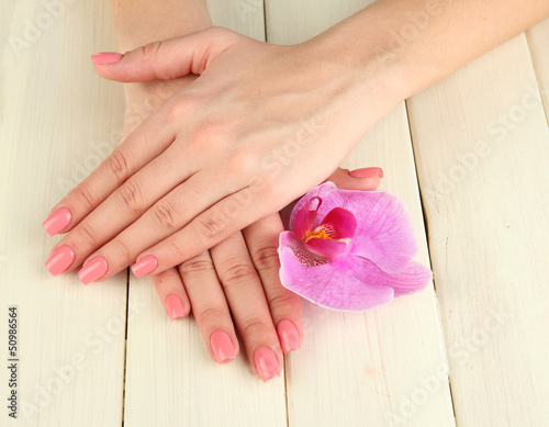 Woman hands with pink manicure and orchid on  wooden background