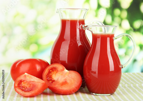 Tomato juice in pitchers on table on bright background © Africa Studio
