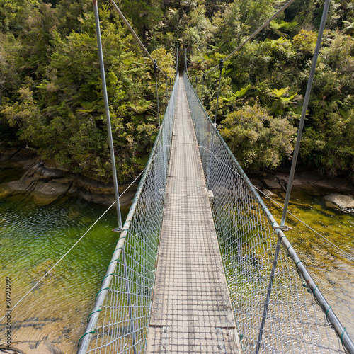 Fototapeta Naklejka Na Ścianę i Meble -  Swing bridge over green jungle river New Zealand