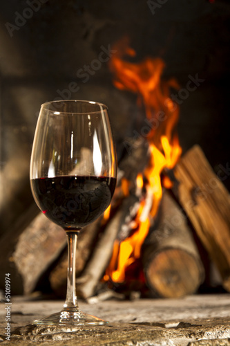 Copa de vino tinto con fuego de fondo.