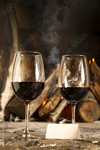 Copas de vino tinto con chimenea y fuego de fondo.