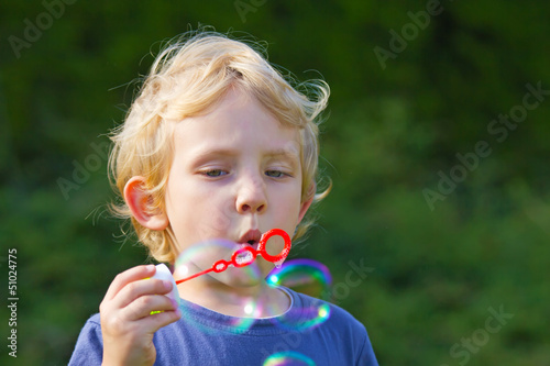 Blond boy making soap bubbles outside