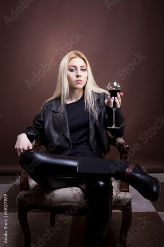 Sensual woman in a vintage chair in leather jacket with a glass