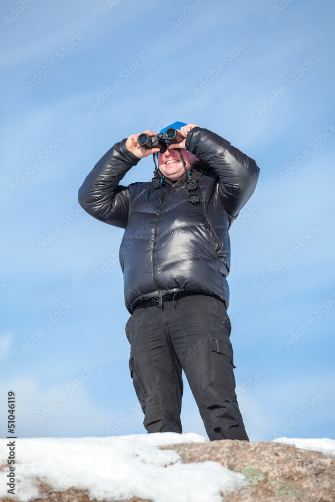 Man standing on rock and looking at binoculars on blue sky