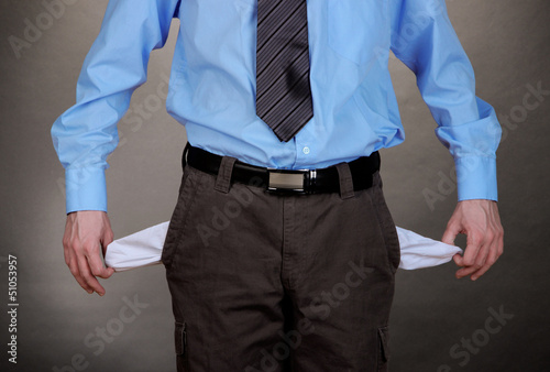 Business man showing his empty pockets, on grey background