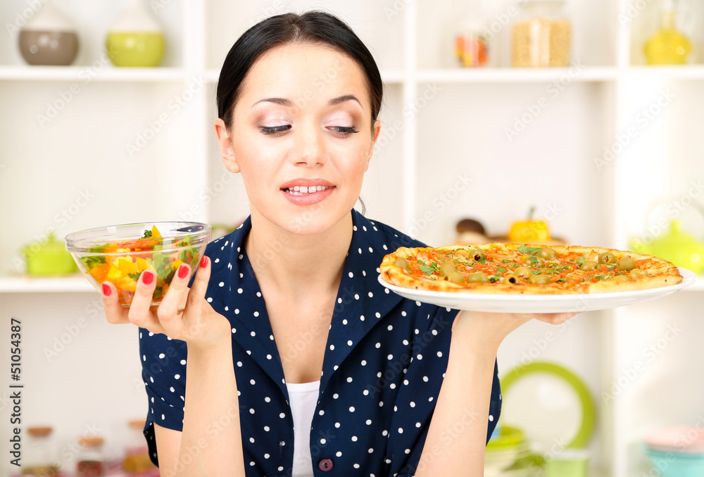 Pretty girl selects pizza or diet on kitchen background Pretty girl selects pizza or diet on kitchen background