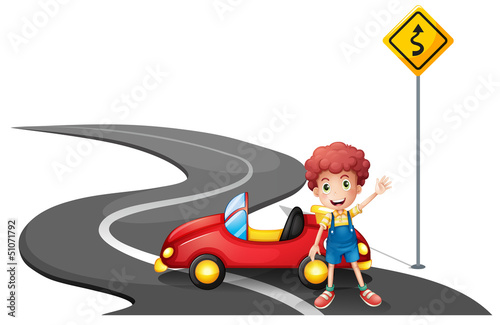 A young boy near a yellow signage with his car