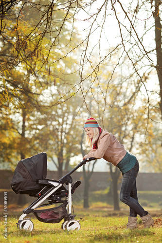 Young mother with a baby carriage walking in a park