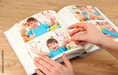 Photos in hands and photo album on wooden table