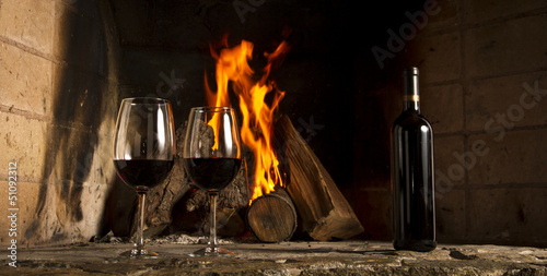 Copa de vino tino con fuego de chimenea de fondo.