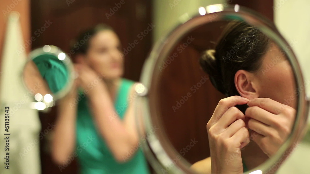 Beautiful woman putting on earrings in bathroom