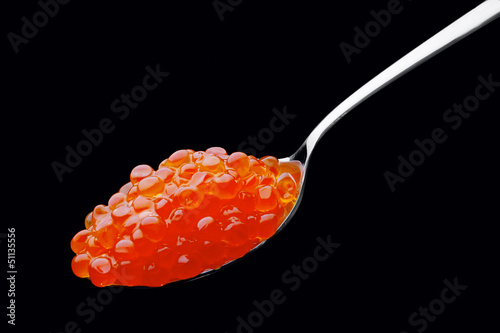 The spoon with red caviar on a black background